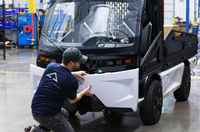 man adjusting front panel of AYRO Vanish low speed vehicle in factory